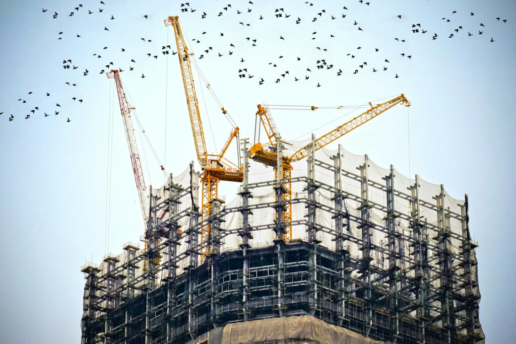High-rise building under demolition, surrounded by scaffolding with multiple cranes positioned for deconstruction.