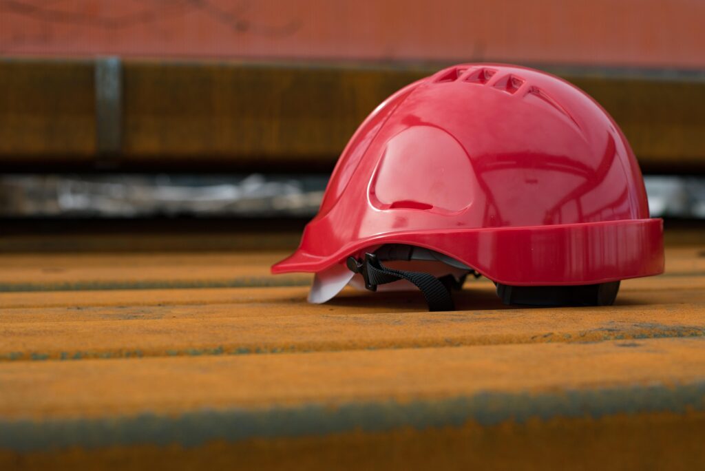 A red hard hat resting on a rusty steel beam at a construction site, symbolizing safety and industrial work.